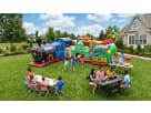 All Aboard" themed inflatable train combo with a slide and climbing area at an outdoor kids' party. The setup includes red and blue seating for children, themed table decor, and professional concession equipment. This premium party attraction is perfect f